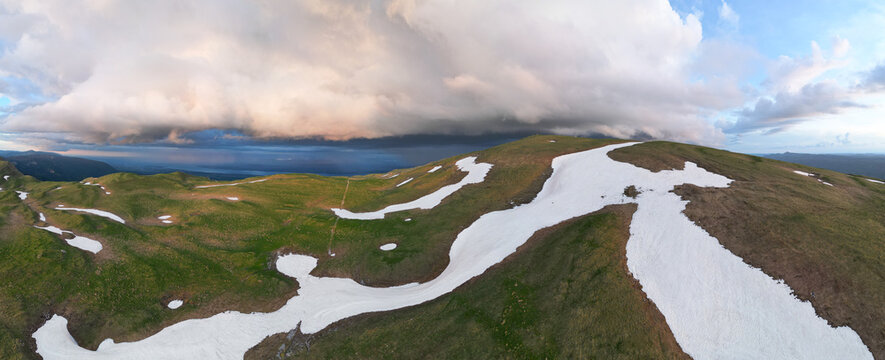 Aerial view of Le Colomby de Gex featuring snow patches on green mountain slopes under dramatic storm clouds in Echenevex, Auvergne-Rhone-Alpes, France.