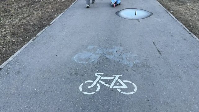 Faded bicycle lane stencil on asphalt, white bike symbol beneath old blue smudge, worn tarmac texture captured in closeup top down