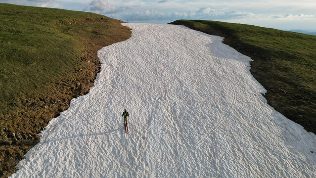 Aerial view of a skier descending a narrow snow patch on the grassy slopes of Le Colomby de Gex under a cloudy sky Echenevex, Auvergne-Rhone-Alpes, France.