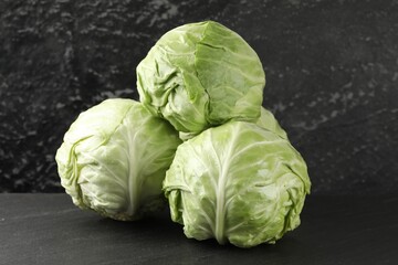 Fototapeta premium Fresh cabbages on black textured table, closeup
