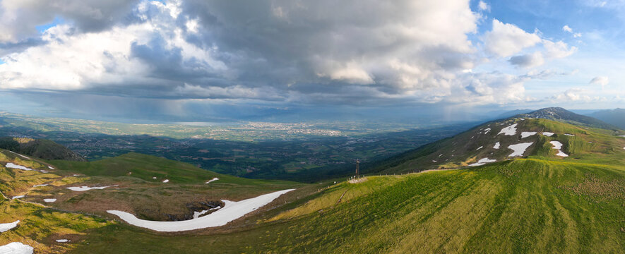 Aerial view of Le Colomby de Gex mountain peak with green slopes and patches of snow overlooking the valley and Lake Geneva, Echenevex, Auvergne-Rhone-Alpes, France.
