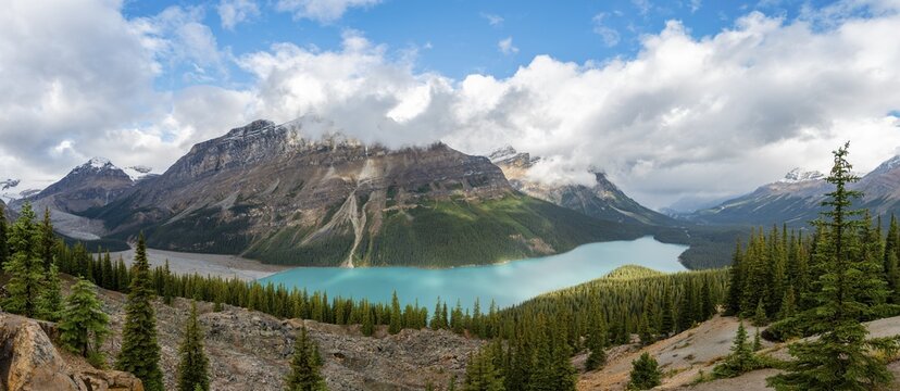 Clouds hanging in mountain peaks, turquoise glacial lake surrounded by forest, Peyto Lake, Rocky Mountains, Banff National Park, Alberta Province, Canada