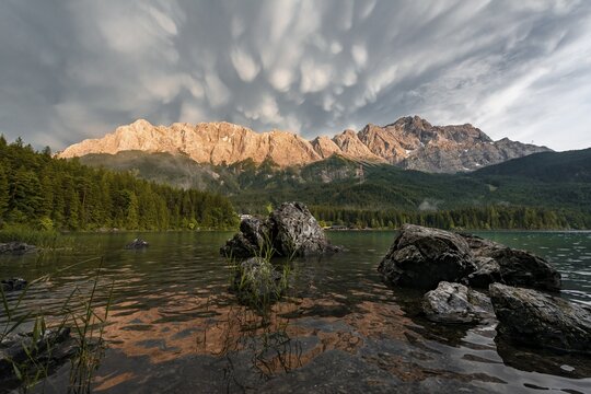 Rocks on the shore, Eibsee lake in front of Zugspitze massif with Zugspitze, sunset, dramatic Mammaten clouds, Wetterstein range, near Grainau, Upper Bavaria, Bavaria