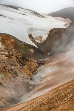 Steaming stream between colourful rhyolite mountains and snowfields, Hveradalir geothermal area, Kerlingarfj&ouml;ll, Icelandic Highlands, Iceland