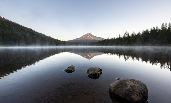Three stones in the water, reflection of the volcano Mt. Hood in the lake Trillium Lake, at sunrise, Oregon, USA