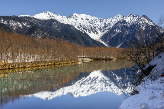 Snow-covered mountains at a lake, Japanese Alps reflected in Taisho Pond, snow-covered Mount Hotaka at the back, Kamikochi, Matsumoto, Nagano, Japan