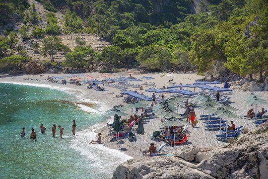 Apella beach, with many people, parasols and surrounding forest, Apella beach, Karpathos, Greece