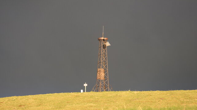 Aerial view of Le Colomby de Gex lattice tower standing on a grassy mountain ridge under a dark dramatic sky Echenevex, Auvergne-Rhone-Alpes, France.