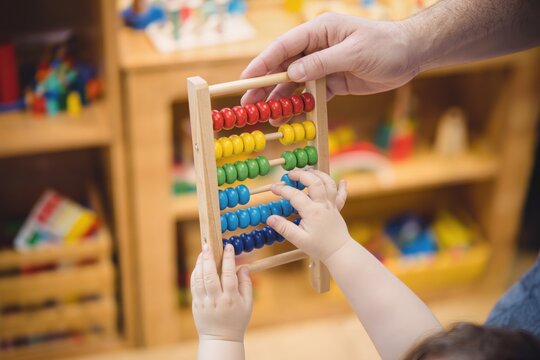 Enfant utilisant un boulier &eacute;ducatif en bois avec un adulte dans une salle de jeux Montessori