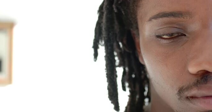 African American man opening eye slowly in bright room backlit by window with dreads, focusing gaze