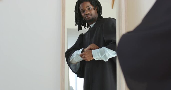 African American man in doorway adjusting cuffs and fastening robe after mirror glance, watch