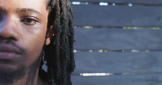 African man dreadlocked blinking and shifting gaze at painted slat fence from sunlight, copy space