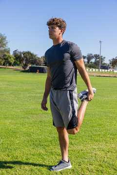 Male performing standing quadriceps stretch on grass athletic field wearing running shoes