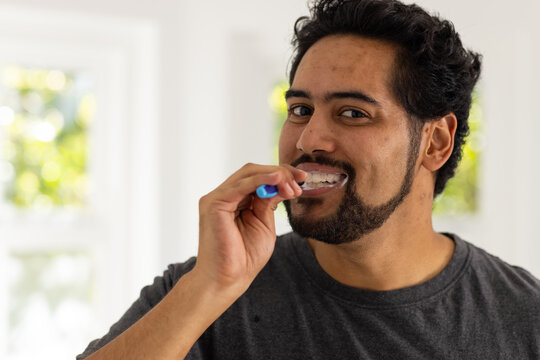 Mid adult African American man brushing teeth with blue-handled toothbrush with foam in bathroom
