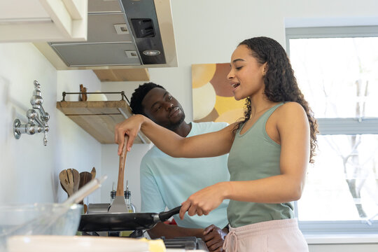 African American couple cooking on gas stove in home kitchen, woman flipping food with wood spatula
