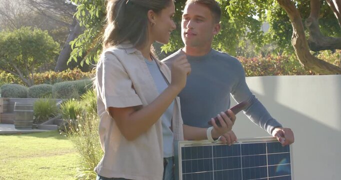 Couple in yard, woman pointing to sun patch while man holding solar panel checking phone placement