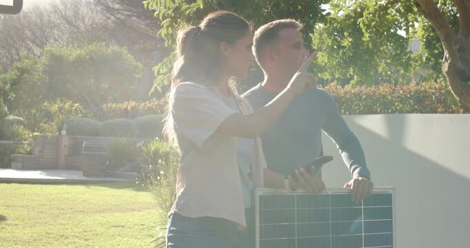 Couple holding solar panel, reacting to glare, checking phone, pointing to lawn, finding placement