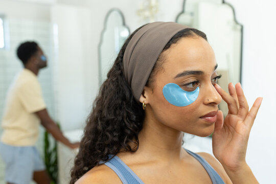 African American couple applying blue hydrogel under-eye patches at bathroom vanity, copy space