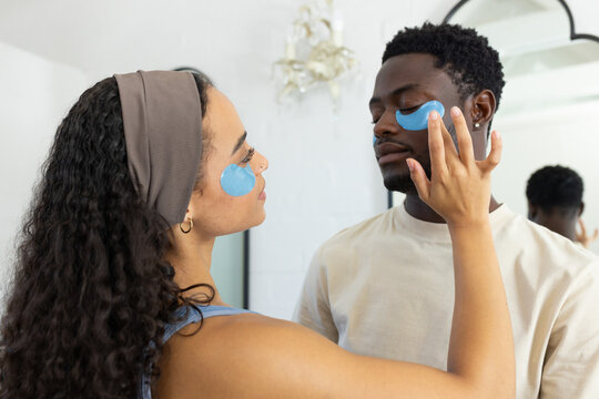 African American couple applying hydrogel patches in bathroom mirror, woman adjusting patch on man