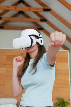 Woman wearing white virtual reality headset reaching forward in living room with wooden wall