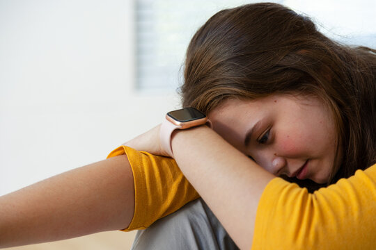 Woman resting head on folded arms, leaning in room with mustard yellow top and smartwatch