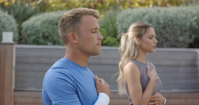 Diverse couple starting breath, placing hands on chest, belly, breathing for calm on patio by fence