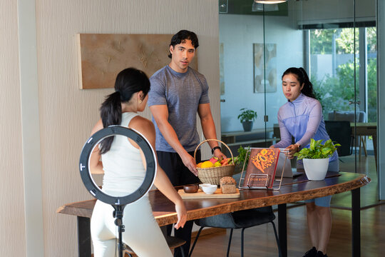 Diverse team positioning fruit basket on table in studio wearing sportswear filming with ring light