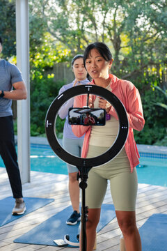 Diverse fitness group in sportswear recording workout on pool deck with ring light, smartphone