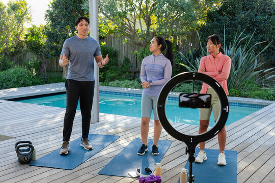 Fitness instructor with two trainees leading outdoor workout on deck by pool with ring light
