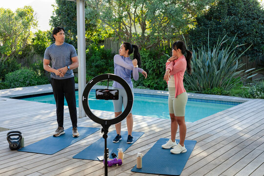 Diverse trainer guiding trainees stretching on blue mats on pool deck, ring light recording