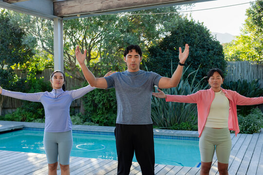 Diverse adults practicing breathing, extending arms on backyard deck beside pool showing smartwatch