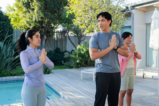 Diverse adults standing on wooden pool deck practicing prayer pose by pool, wearing sportswear