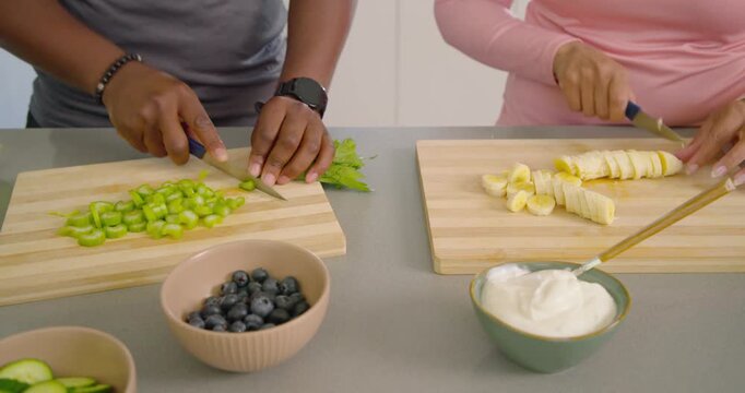 African American couple chopping celery and slicing banana at counter making yogurt bowls on boards