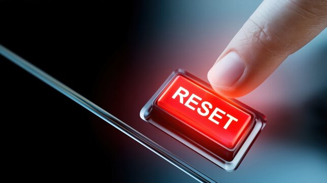 A finger presses a glowing RESET button on a modern control panel. Dramatic lighting and dark background illustrate recovery, restart, and fresh start concepts.