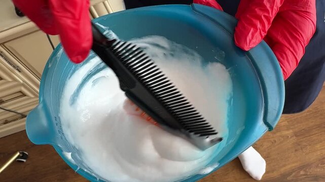Hair dye mixing with comb in salon coloring bowl and gloves during bleach preparation by hairdresser. Professional beauty process for hair treatment, highlights and blonding services.