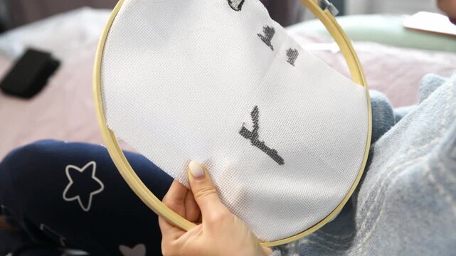 Close up view of hand stitching black thread design on fabric with wooden embroidery hoop indoors