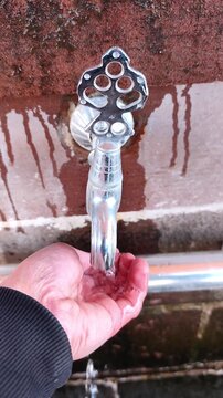 Vertical static shot of a person's palm filling with fresh water from a traditional ornate metal tap at a mosque fountain.