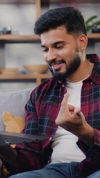Handsome indian man working on laptop computer while video calling. Browsing lnternet, using social networks, having fun in flat. Slow motion.