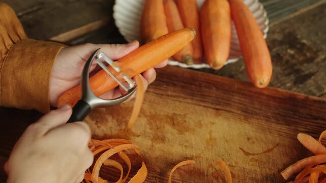 Hands peel carrot with a vegetable peeler. Cooking process. Raw food diet.