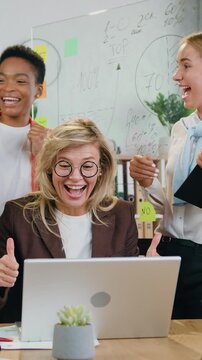 Excited and happy the team of four successful colleagues of women winner looking at laptop and celebrates online success at briefing table in office room. Slow motion