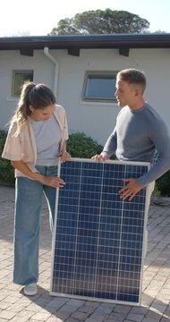 Vertical video: Diverse couple placing upright solar panel on driveway, inspecting for roof fit