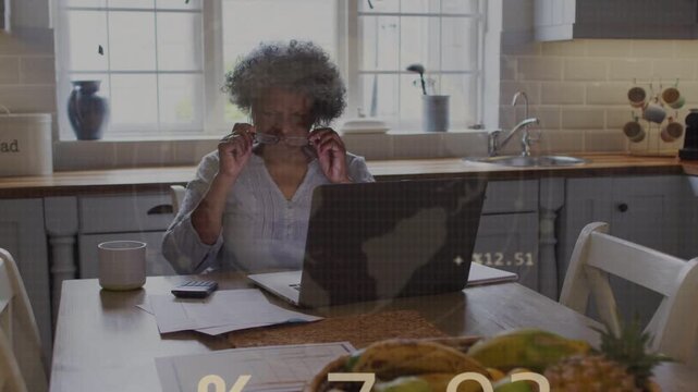 Senior woman adjusting specs while reviewing budget at laptop causing data charts covering woman