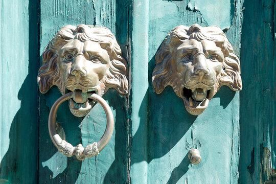 Lion head door knockers on a weathered turquoise door