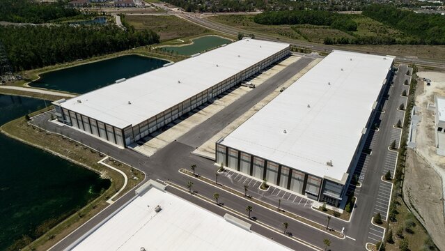 Aerial view of large modern industrial warehouses with white roofs, parking lots, and retention ponds in World Golf Village, Florida, United States.