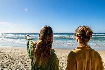 Women standing on beach pointing at ocean waves © unai