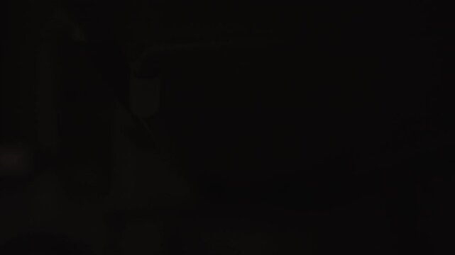 Close-up hands of unrecognizable person reaches into dark space to switch on long, thin tube light, light illuminates area briefly before being turned off again, returning scene to complete blackness.