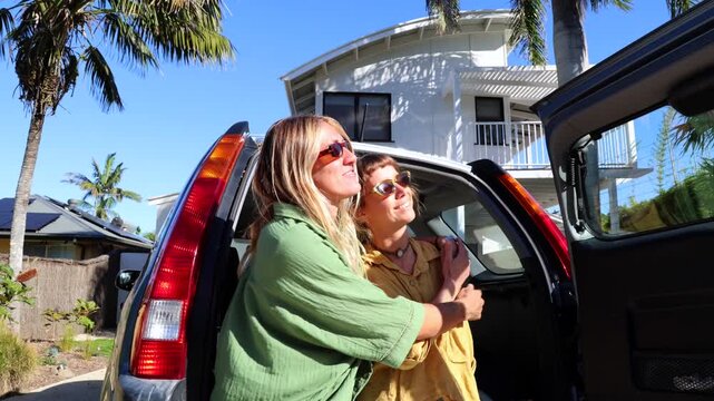 Two young smiling women surfers enjoying a sunny day on a tropical vacation, standing by their car and hugging before heading to the beach for a surf session in beautiful australia