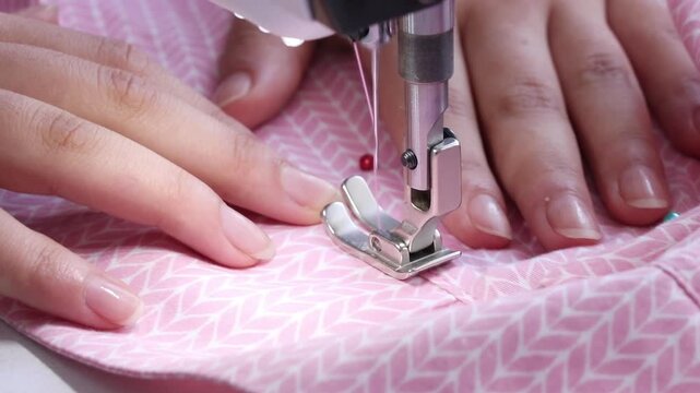 Сlose up of seamstress fingers sewing pink fabric on machine tailoring process garment creation work