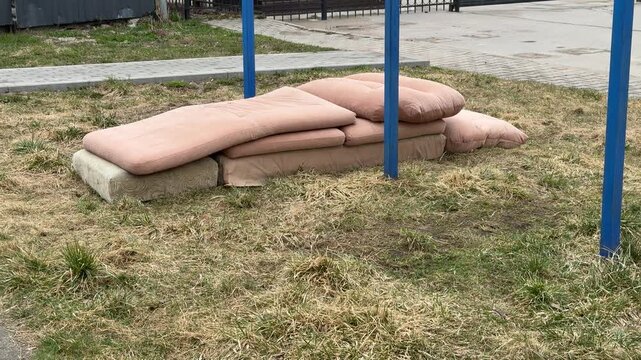 Courtyard pullup bar with sofa mats, spring day blue metal turnstile, stacked pink cushions from old sofa tossed on grass