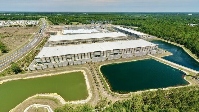Aerial view of industrial warehouses on Foundry Lane with retention ponds and a highway surrounded by dense green forest in World Golf Village, Florida, United States.